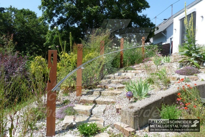 Der Handlauf für die Naturstein-Gartentreppe ist an besonders witterungsbeständigen Pfosten aus Corten-Stahl befestigt. Durch die Materialien und geschwungene Form fügt sich das Treppengeländer besonders natürlich in die Landschaft.